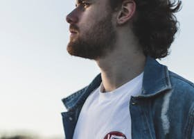 Profile of a fashionable man in a denim jacket outdoors, exuding a serious demeanor.