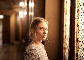 Portrait of a woman in an elegant, warm-toned room with stained glass window. Artistic and serene.