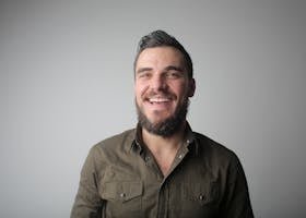 Portrait of a bearded man smiling joyfully in a casual studio setting.