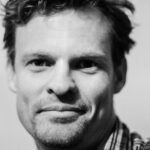 Close-up black and white portrait showcasing a smiling man with facial hair.